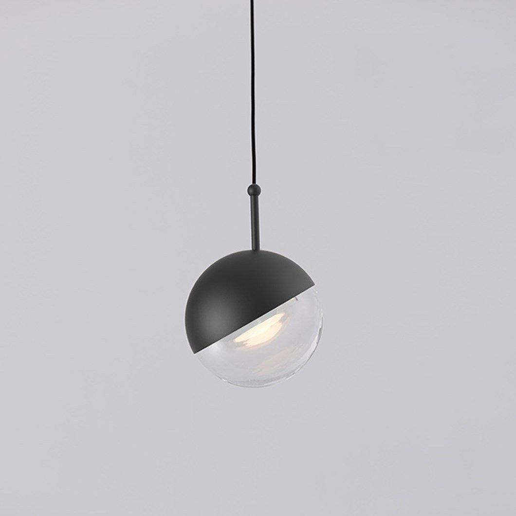 Close view of a matt black Clérachic globe pendant, its black half-cap over a clear glass half with a warm LED inside.