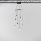 Clérachic ring chandelier with small rose gold globe pendants, hung from a black ceiling plate under a metal truss.