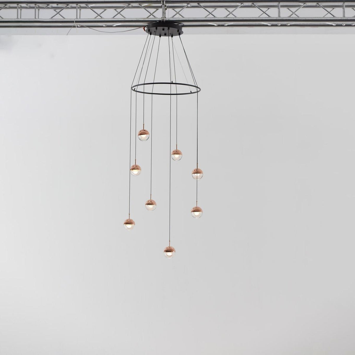 Clérachic ring chandelier with small rose gold globe pendants, hung from a black ceiling plate under a metal truss.