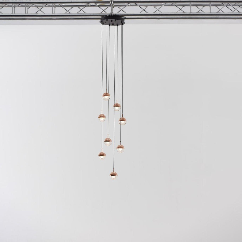 Narrow cluster of small rose gold Clérachic globe pendants on cords of varied length, hung from a black ceiling plate.
