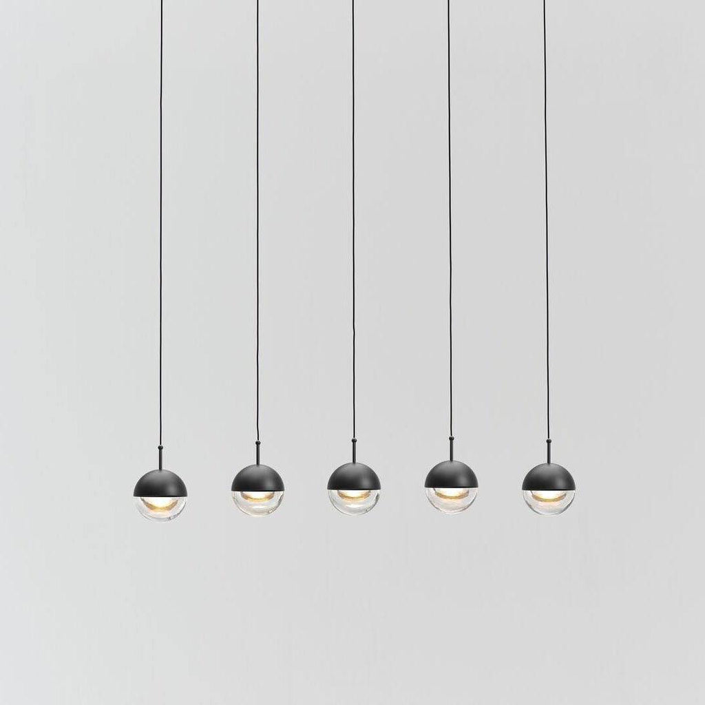 Five small matt black Clérachic globe pendants with clear lower halves hung in a row against a pale grey wall.