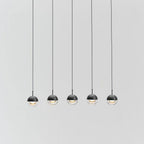 Five small matt black Clérachic globe pendants with clear lower halves hung in a row against a pale grey wall.