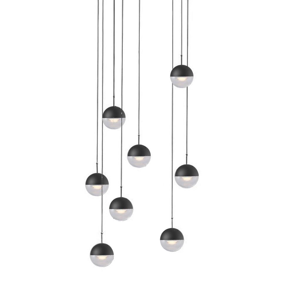 Cluster of nine matt black Clérachic globe pendants with clear lower halves, hung at varied heights on a white backdrop.