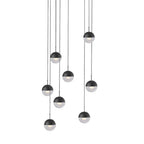 Cluster of nine matt black Clérachic globe pendants with clear lower halves, hung at varied heights on a white backdrop.