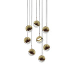 Cluster of nine gold-finish Clérachic globe pendants hung close together on cords of varied length, on a white backdrop.