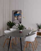 Unlit gold-finish Clérachic globe pendants hung at varied heights in front of a framed portrait, above a grey dining table.