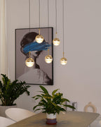 Close view of lit gold-finish Clérachic globe pendants beside a framed portrait with a blue brushstroke, above a potted plant.