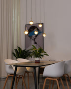 Lit gold-finish Clérachic globe pendants at varied heights by a framed portrait, above a dark table with white chairs.