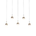 Five small gold-toned Clérachic globe pendants hung at staggered heights on long thin cords, on a white backdrop.