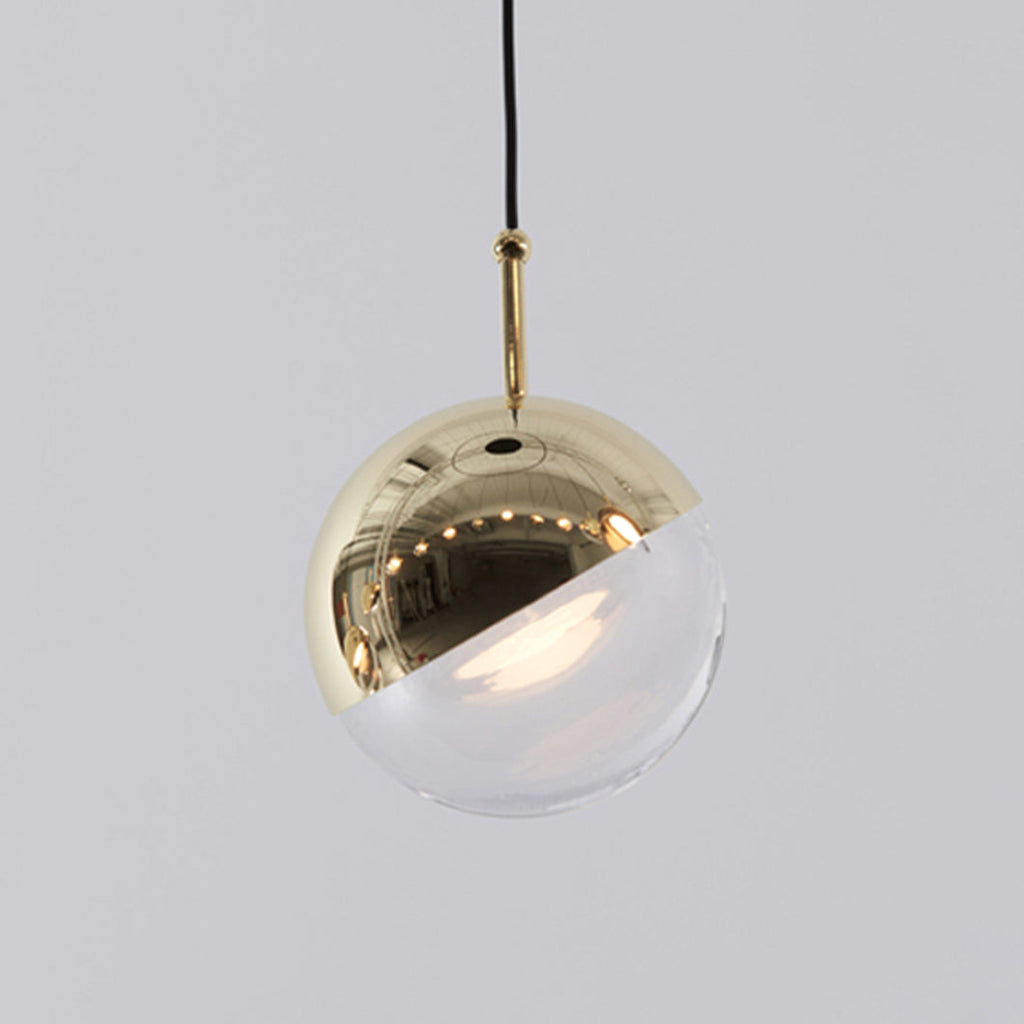 Close view of a pale gold-finish Clérachic globe pendant, its mirror-polished half-cap over a clear glass half.