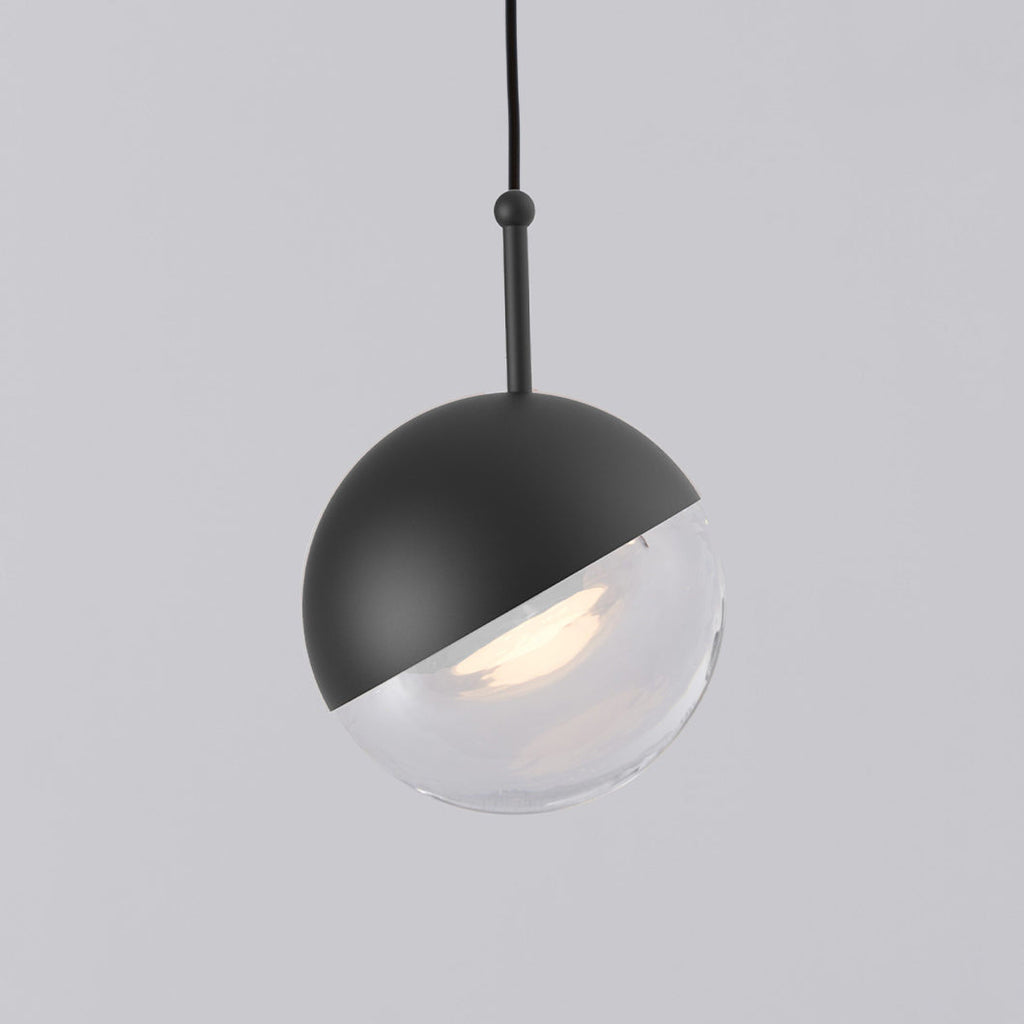 Close view of a matt black Clérachic globe pendant with a short black stem and a clear glass lower half.