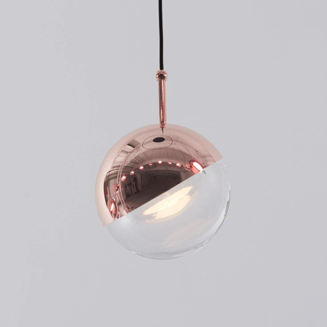 Close view of a rose gold Clérachic globe pendant, its mirror-polished half-cap over a clear glass half.