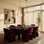 Clérachic two brass-framed frosted glass pendants lit warm above a dark dining table with burgundy chairs and sheer curtains.