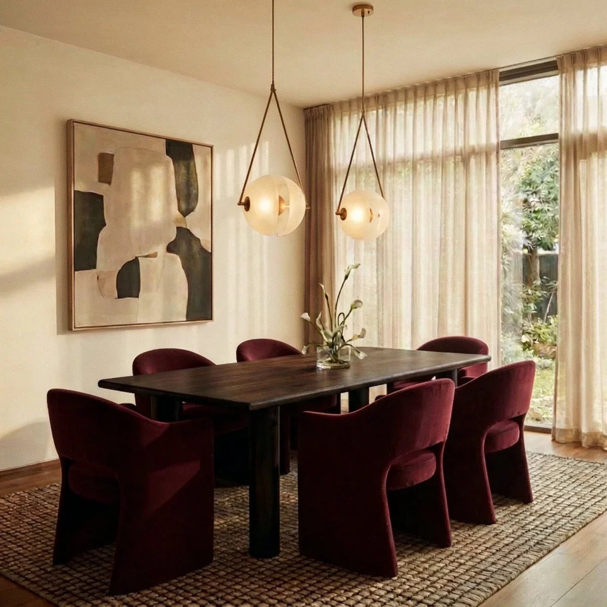 Clérachic two brass-framed frosted glass pendants lit warm above a dark dining table with burgundy chairs and sheer curtains.