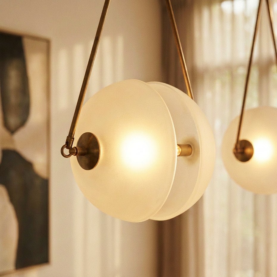 Clérachic close-up of a frosted glass half-disc pendant glowing warm, with a brass cap and thin brass frame arms.