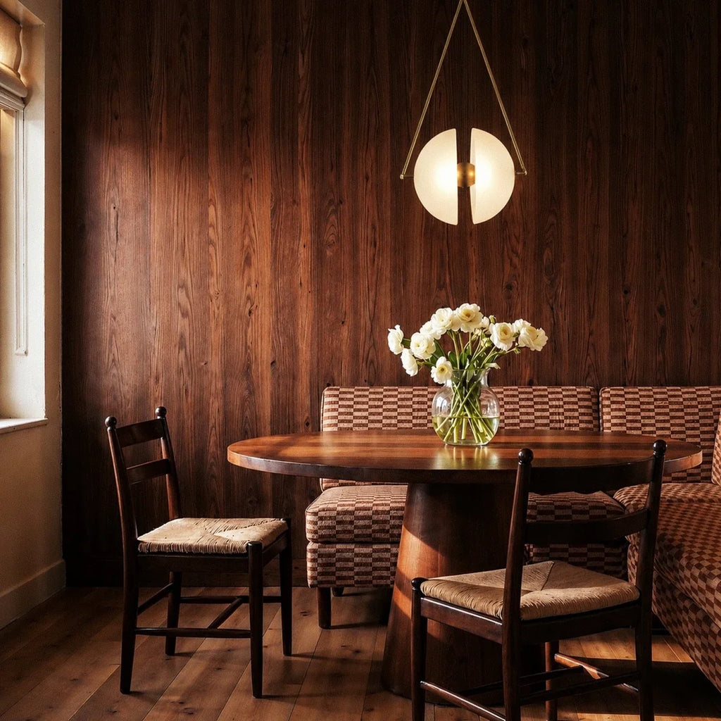 Clérachic brass-framed pendant with split frosted glass discs glowing over a round table in a timber-panelled dining nook.