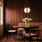 Clérachic brass-framed pendant with split frosted glass discs glowing over a round table in a timber-panelled dining nook.