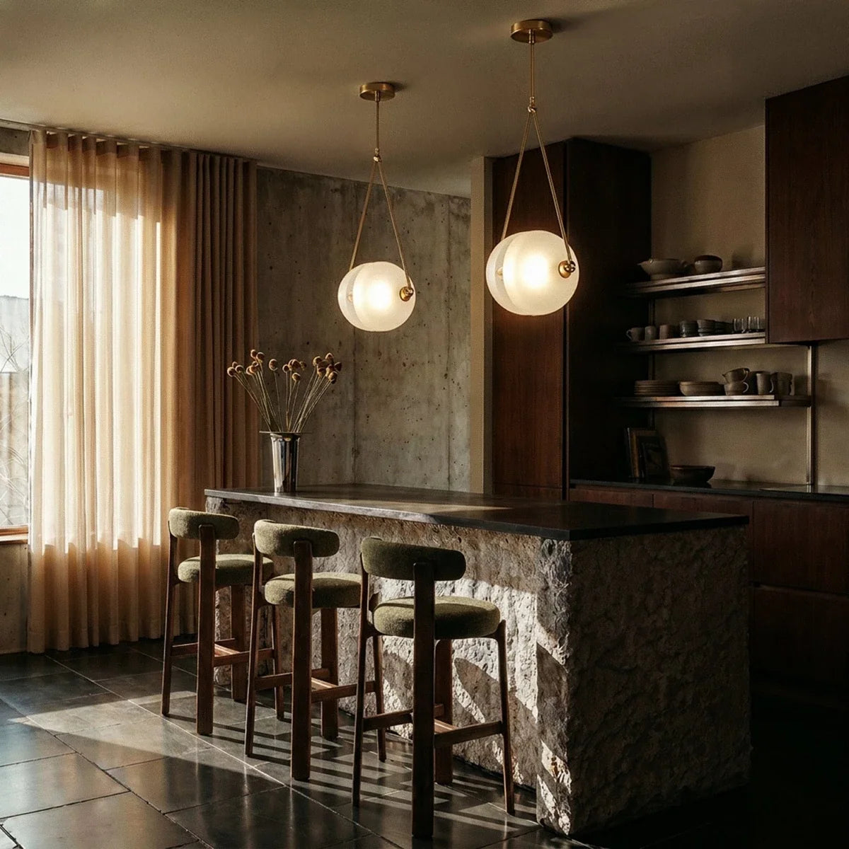 Clérachic two brass-framed frosted glass pendants lit warm above a stone-clad kitchen island with upholstered stools.