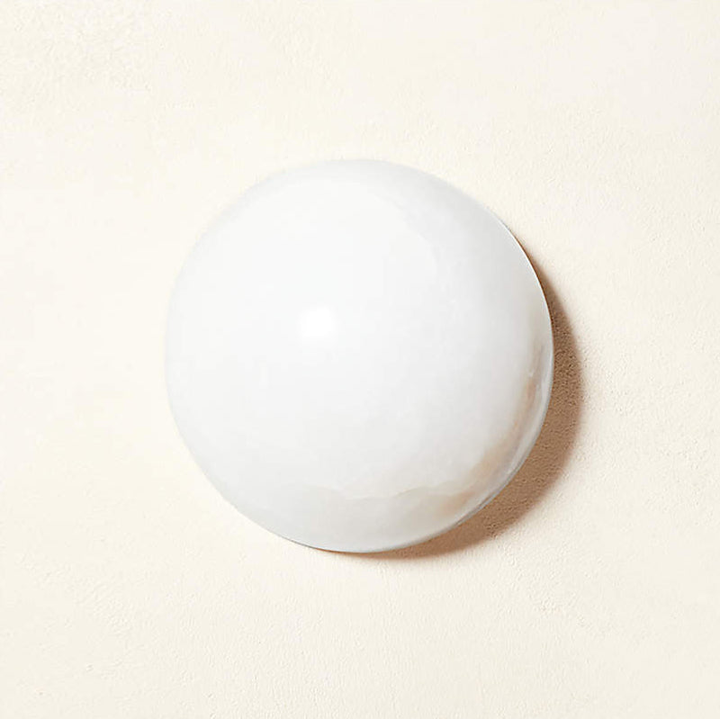 Clérachic Half-Dome Alabaster Wall Sconce unlit on cream plaster, its chalk-white stone face casting a soft shadow.
