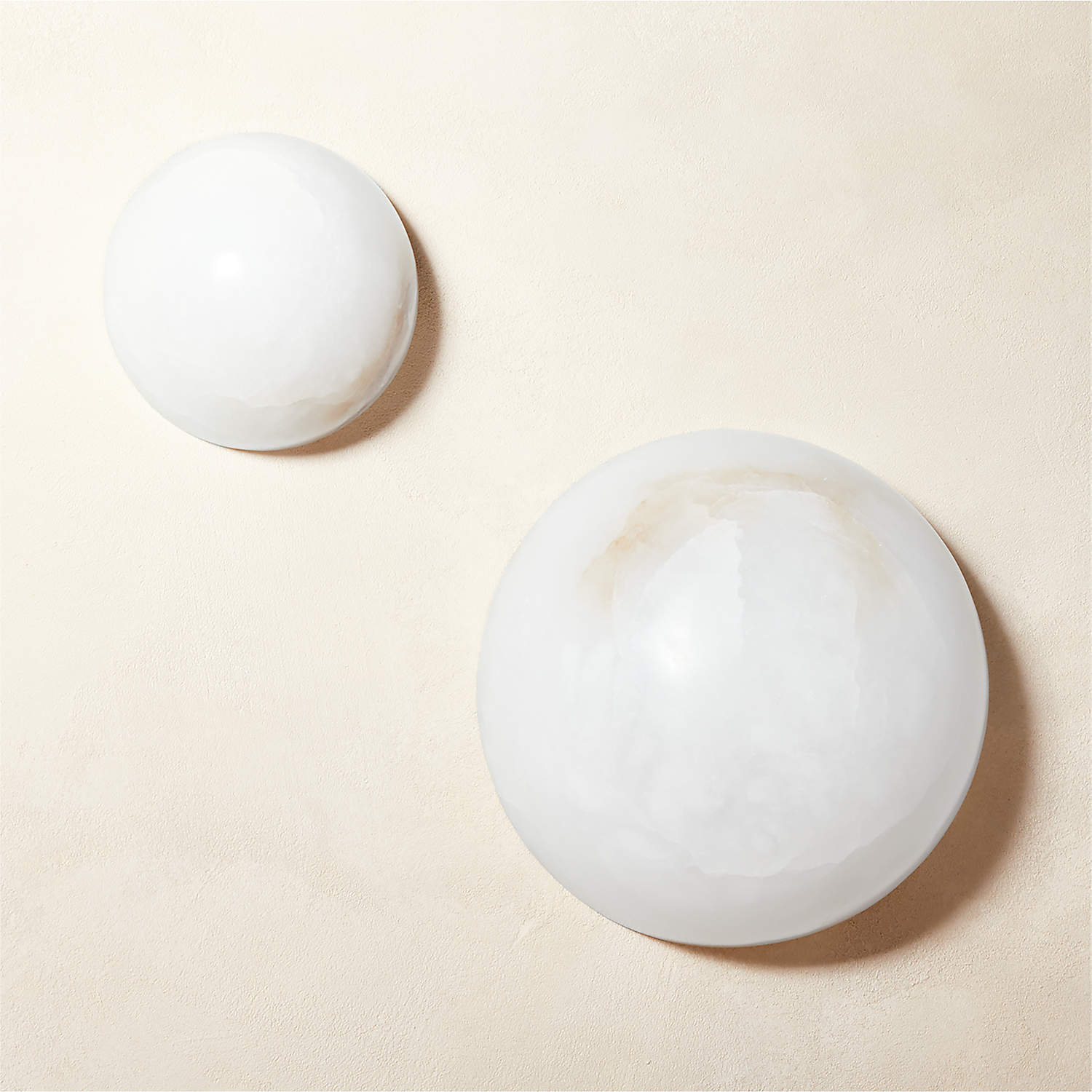 Both sizes of the Clérachic Half-Dome Alabaster Wall Sconce unlit side by side on plaster, the compact dome above the larger one.