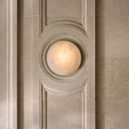 Clérachic Half-Dome Alabaster Wall Sconce lit inside a carved limestone panel, the warm stone face seated in a circular recess.