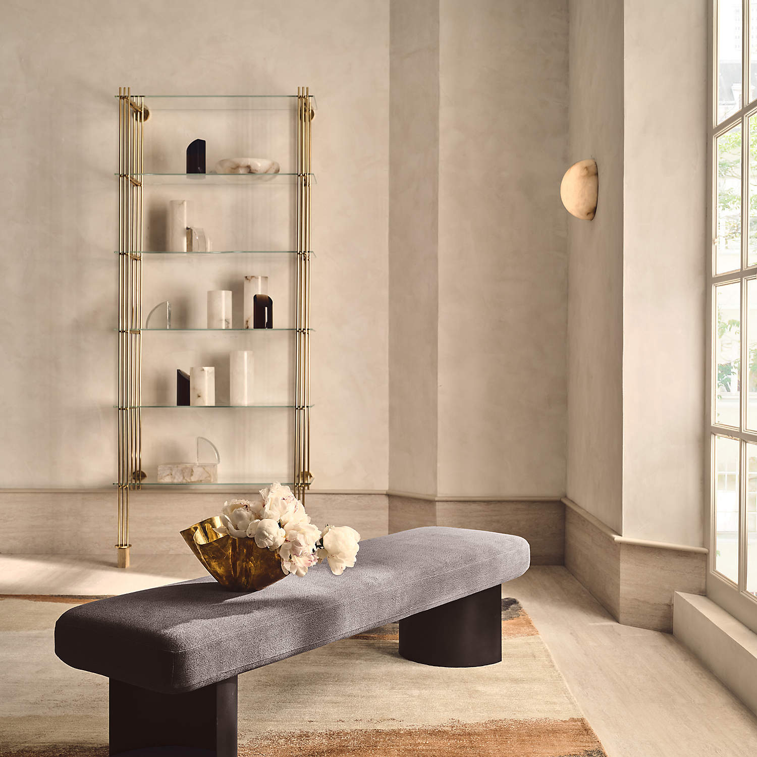 A Clérachic Half-Dome Alabaster Wall Sconce on the plaster wall of a bright living room, above a bench beside a tall window.