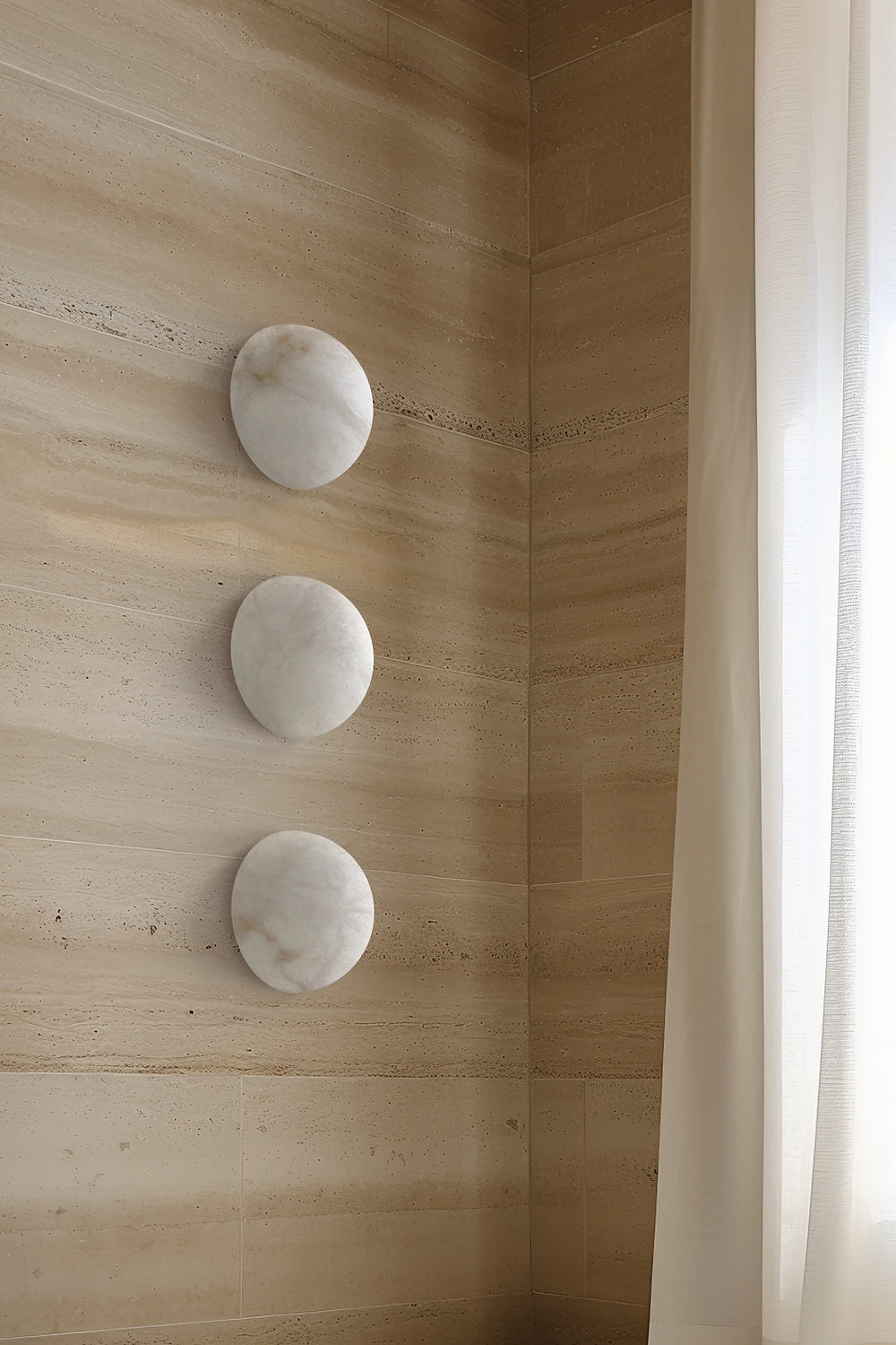 Three Clérachic Half-Dome Alabaster Wall Sconces stacked down a travertine wall beside a sheer curtain in daylight.