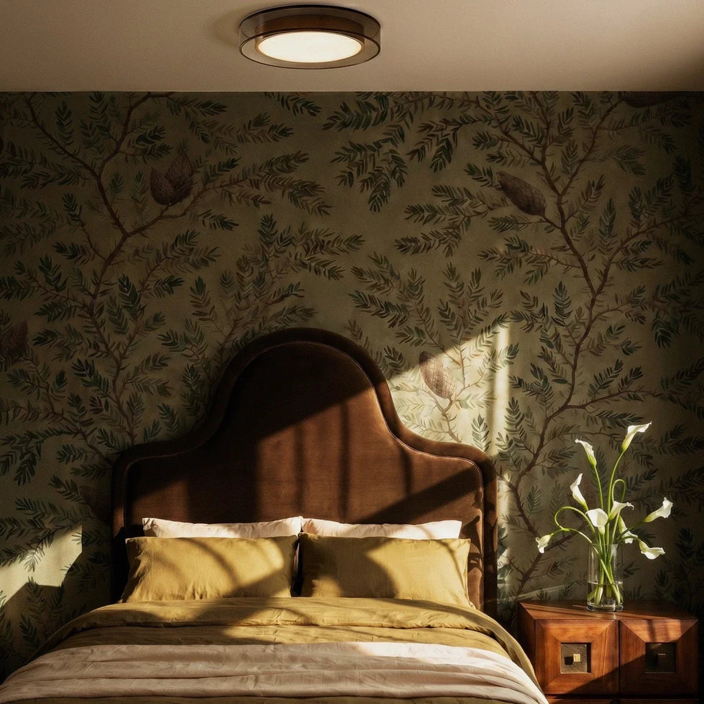 Clérachic halo ring ceiling light glowing above a bed with botanical wallpaper and a dark upholstered headboard.