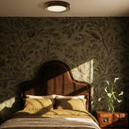 Clérachic halo ring ceiling light glowing above a bed with botanical wallpaper and a dark upholstered headboard.