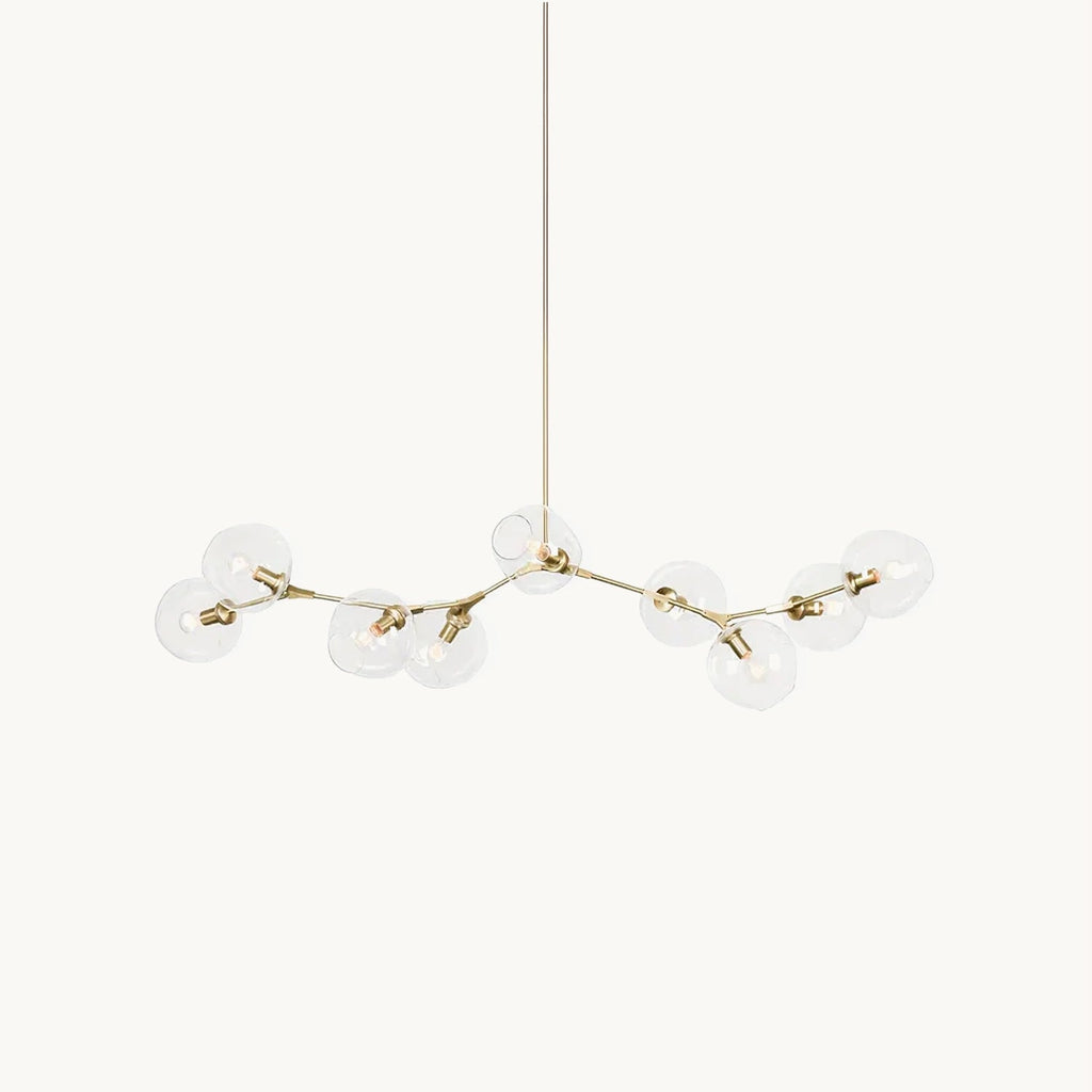 A Clérachic chandelier on a plain white backdrop, with clear glass globes on slim gold arms branching from a long central rod.
