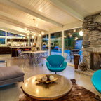 Clear glass globes of this Clérachic chandelier hang over a round brass table in an open living room with a stone fireplace.