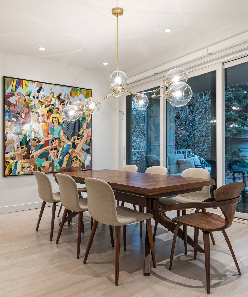 This Clérachic chandelier hangs over a walnut dining table, its clear glass globes reflecting a bright painting on the wall.