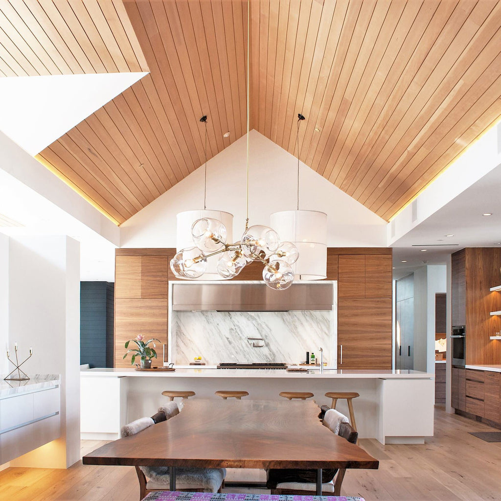 Under a vaulted timber ceiling, this Clérachic chandelier hangs above a long wooden dining table, with white shades nearby.
