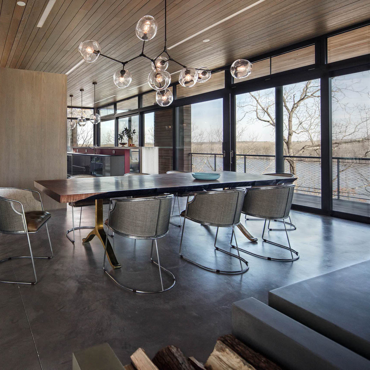 Clear glass globes of this Clérachic chandelier hang from black arms in a dark-floored dining room with tall glass doors.