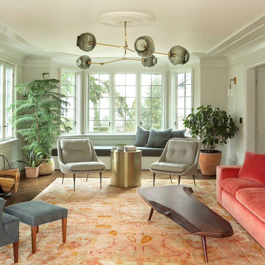 Smoked-glass globes on brass arms make up this Clérachic chandelier, hanging above a coral sofa and an orange patterned rug.