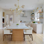 This Clérachic chandelier in gold and clear glass hangs over a white marble kitchen table, with open shelves and wall lights behind.