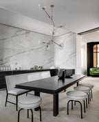 Slim gold arms and clear globes of this Clérachic chandelier hang over a black dining table, set against a veined marble wall.