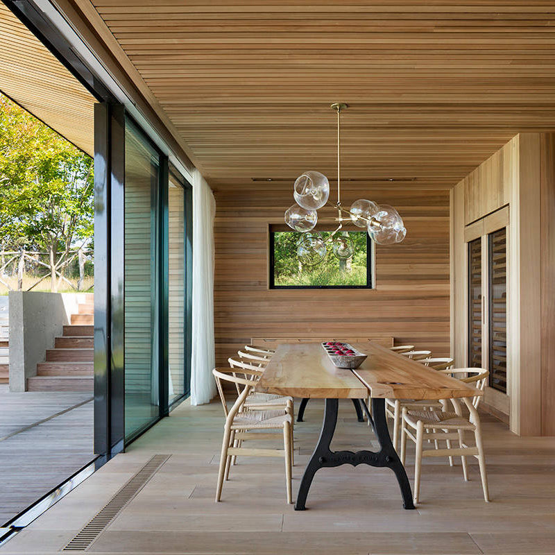 Clear glass globes cluster in this Clérachic chandelier over a long wooden table, in a dining room lined with cedar boards.