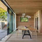 Clear glass globes cluster in this Clérachic chandelier over a long wooden table, in a dining room lined with cedar boards.