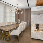 Clear globes on gold arms make up this Clérachic chandelier, hung above a live-edge dining table with cream chairs beside a marble wall.