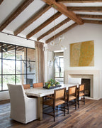 This Clérachic chandelier hangs from a rafted ceiling above a stone-topped dining table, with a large yellow painting behind it.
