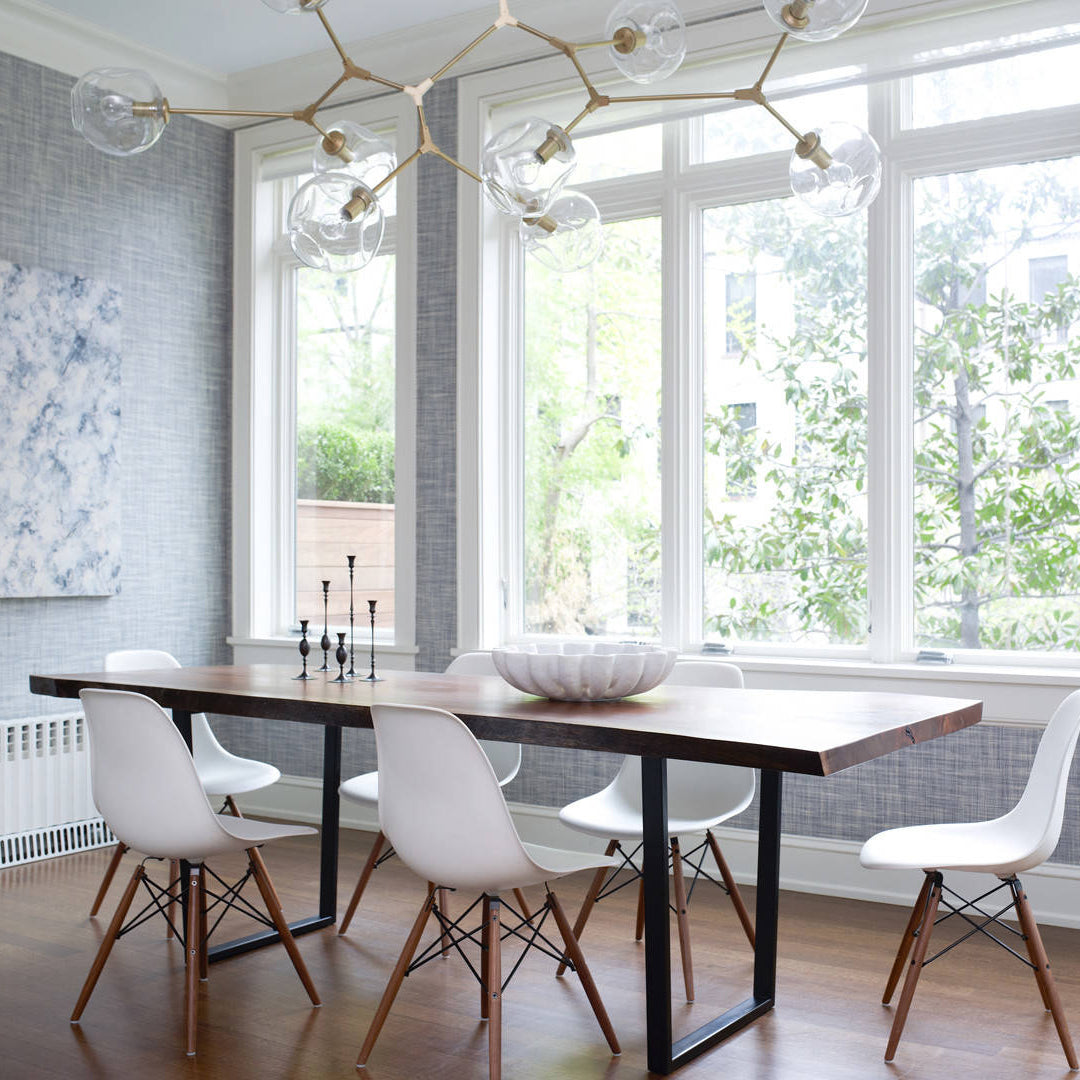 Clear globes along pale metal arms of this Clérachic chandelier hang before tall white windows above a long wooden table.