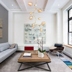 This tall Clérachic chandelier in gold and amber-tinted glass hangs in a white living room beside a large wall artwork.
