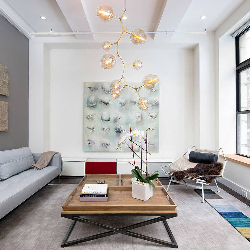 This tall Clérachic chandelier in gold and amber-tinted glass hangs in a white living room beside a large wall artwork.