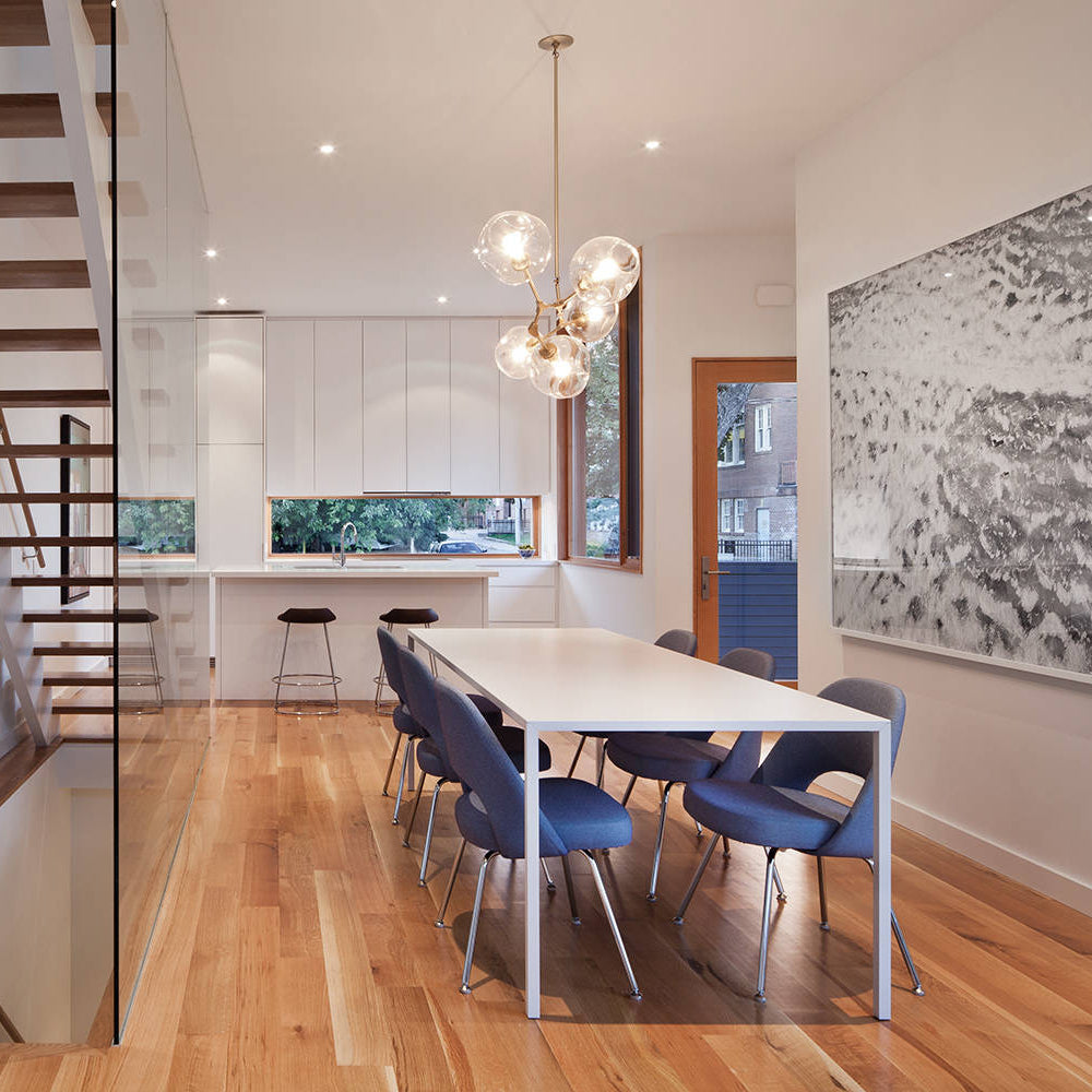 A cluster of clear globes forms this Clérachic chandelier, hanging in an open kitchen and dining room with a bright wood floor.
