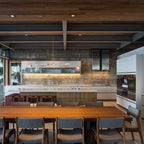 A long horizontal Clérachic chandelier with clear globes hangs far back in a wide kitchen, with a timber ceiling above.