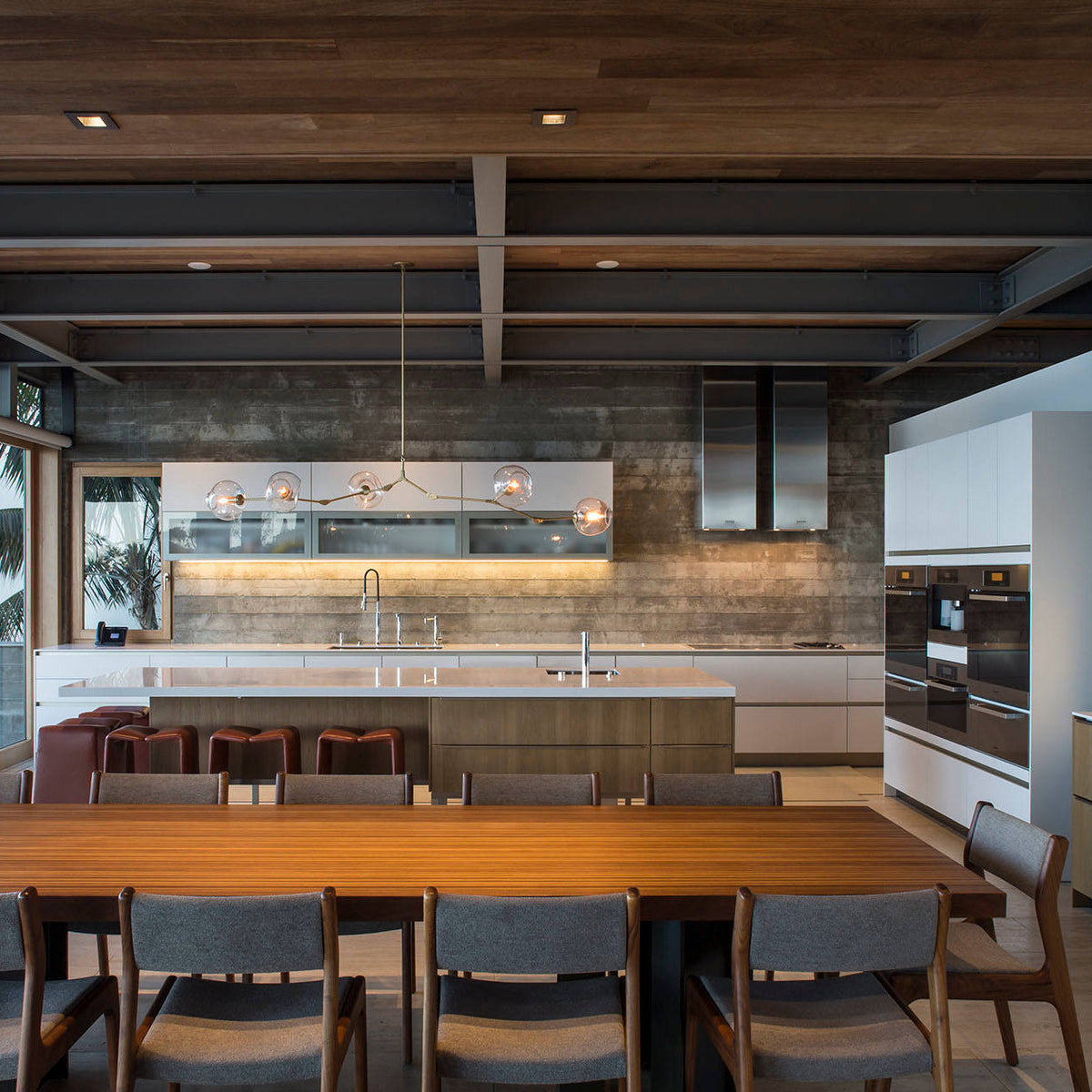 A long horizontal Clérachic chandelier with clear globes hangs far back in a wide kitchen, with a timber ceiling above.