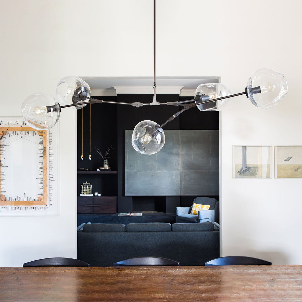 Close view from below of this Clérachic chandelier in black, its clear globes hanging above a wooden table, with a dark alcove behind.