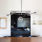 Close view from below of this Clérachic chandelier in black, its clear globes hanging above a wooden table, with a dark alcove behind.