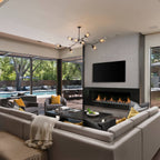 A Clérachic chandelier with black arms and clear globes hangs over a large sectional sofa and a linear fireplace in a wide living room.